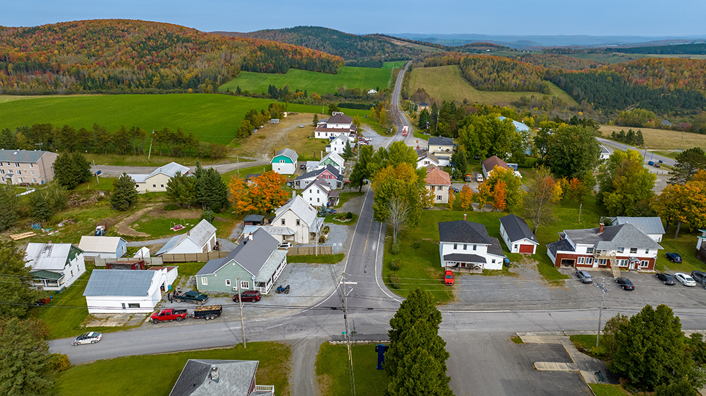 Vue aérienne par drone d’un village et de son environnement naturel démontrant la diversité des projets nécessitant une approche sur mesure.